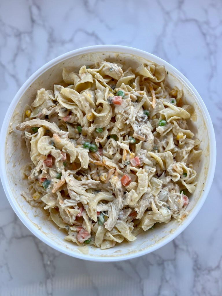 A bowl filled with the filling for chicken noodle casserole on a marble counter