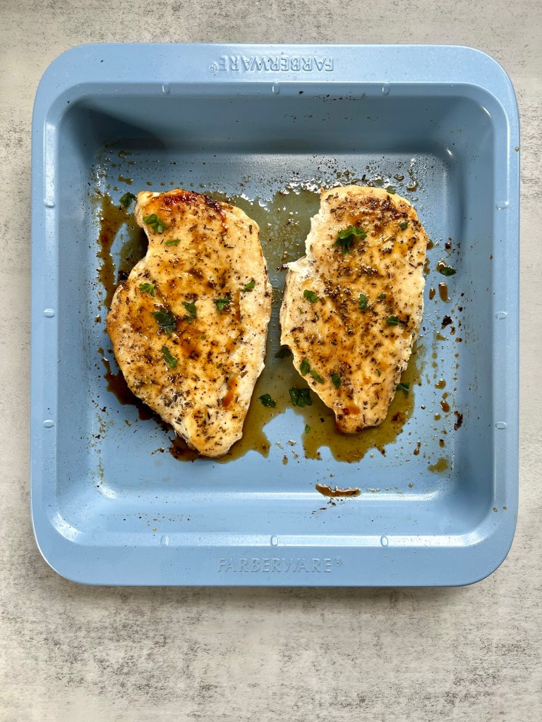 Two oven baked chicken breasts in a blue baking pan