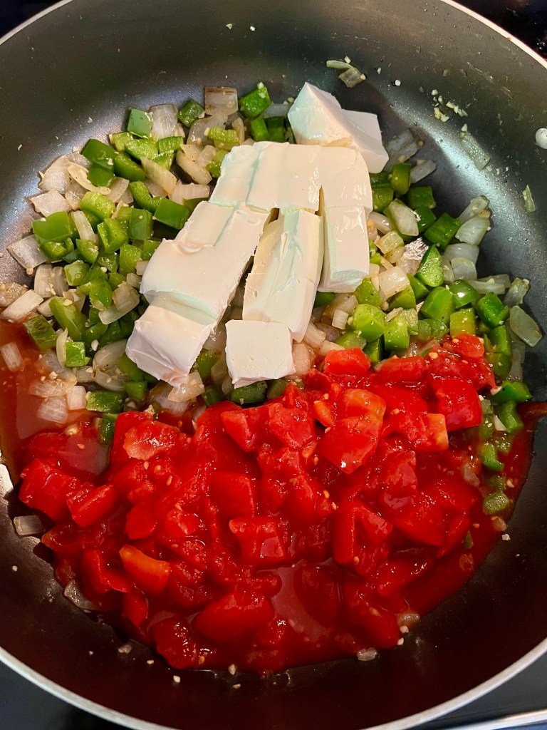 A large skillet on the stove with ingredients for chicken spaghetti cooking