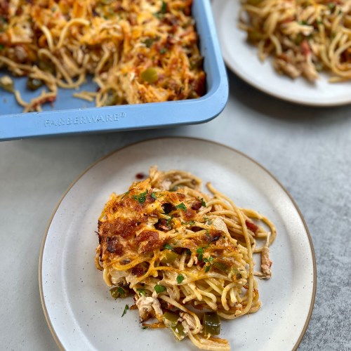 A plate of chicken spaghetti in front of a blue pan filled with it and another plate behind