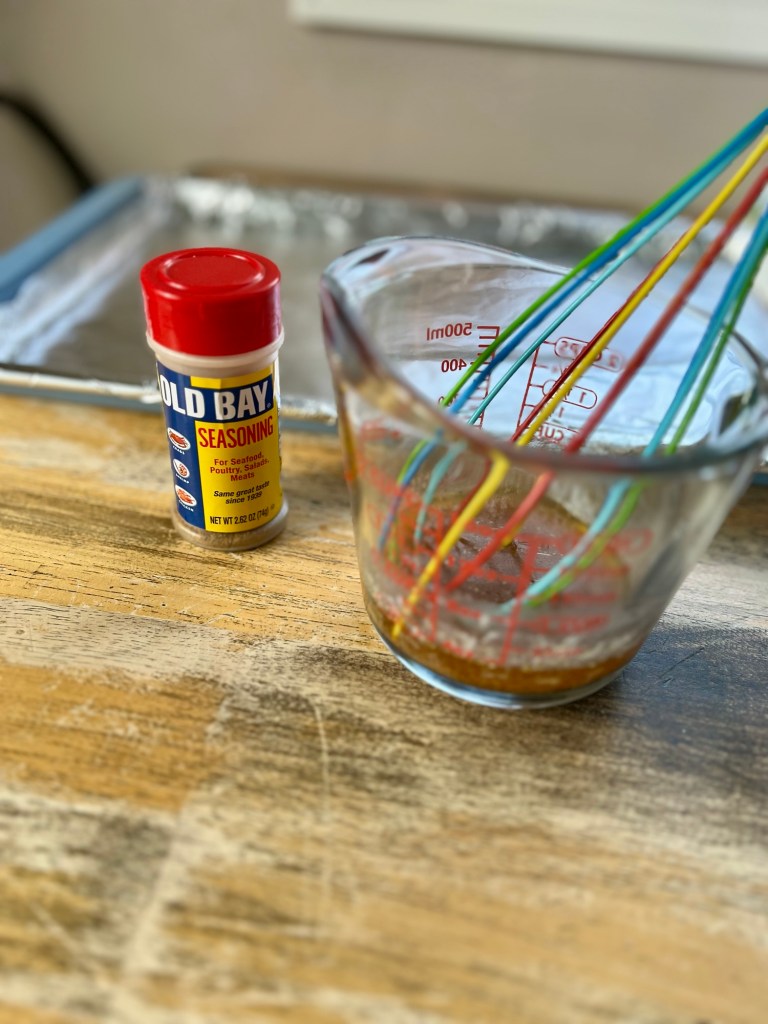 A measuring cup filled with melted butter and seasonings with some old bay next to it on the table