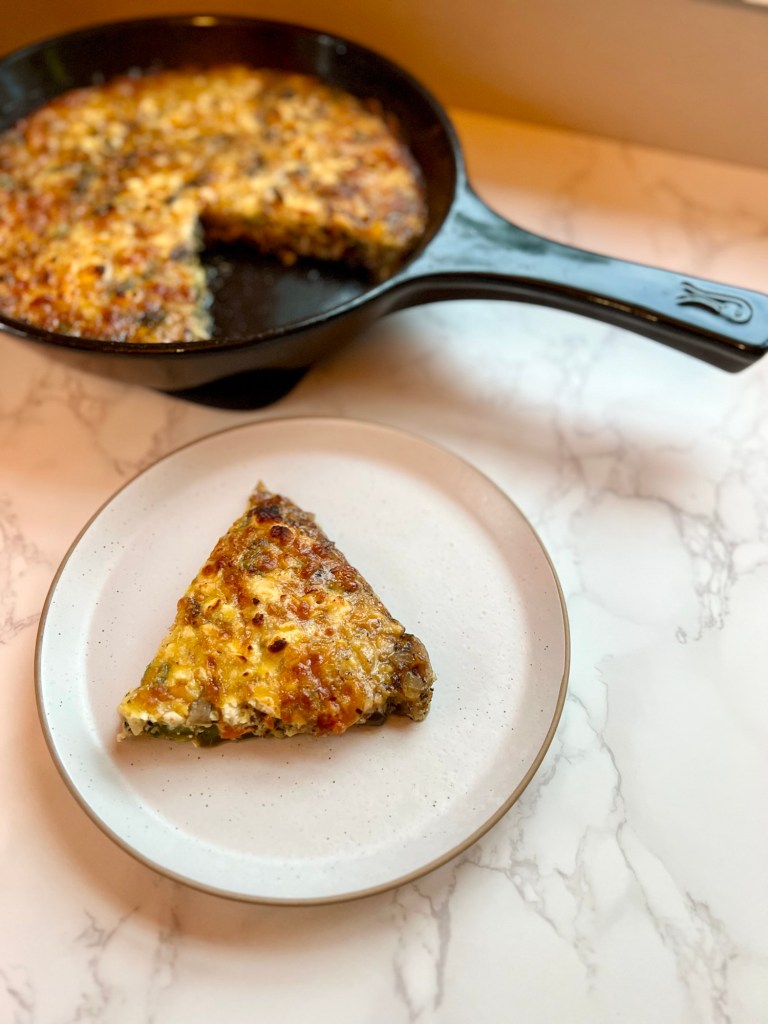 Sausage and veggie frittata in an Xtrema pan with a slice of it on a white plate in front of it