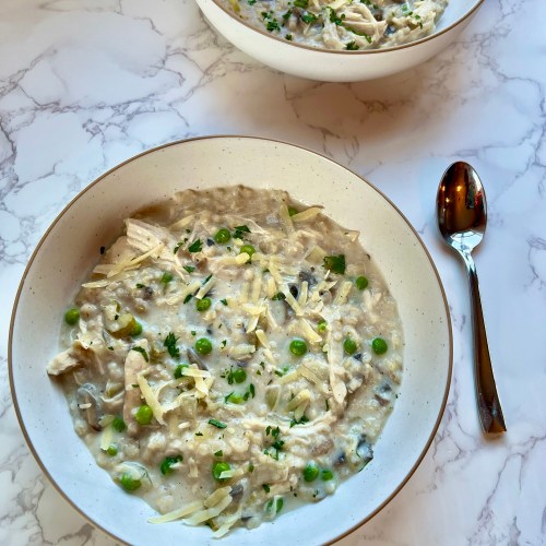 A big bowl filled with soup with another bowl behind it and a spoon next to it