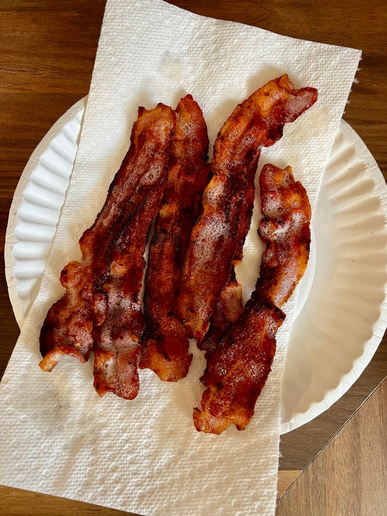Cooked bacon on a paper plate with paper toweling underneath