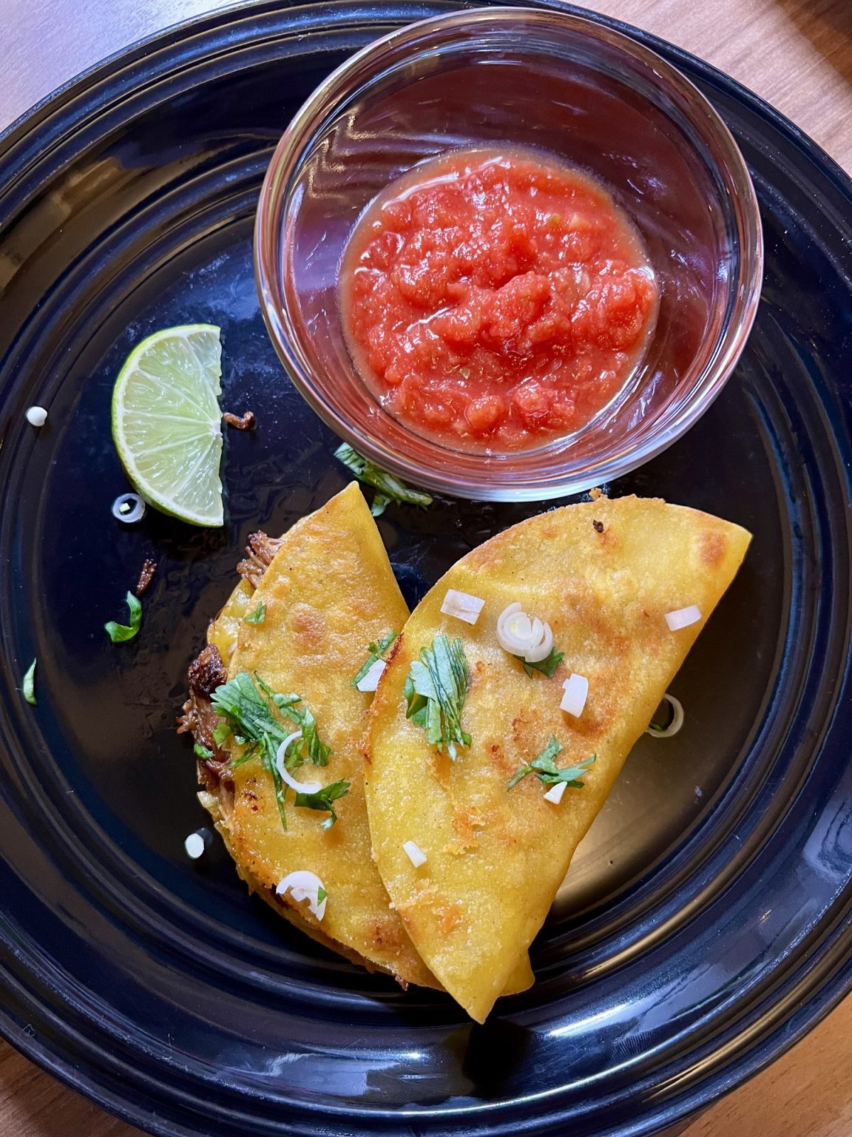 Fried Pulled Pork Tacos on a black plate with a side of salsa
