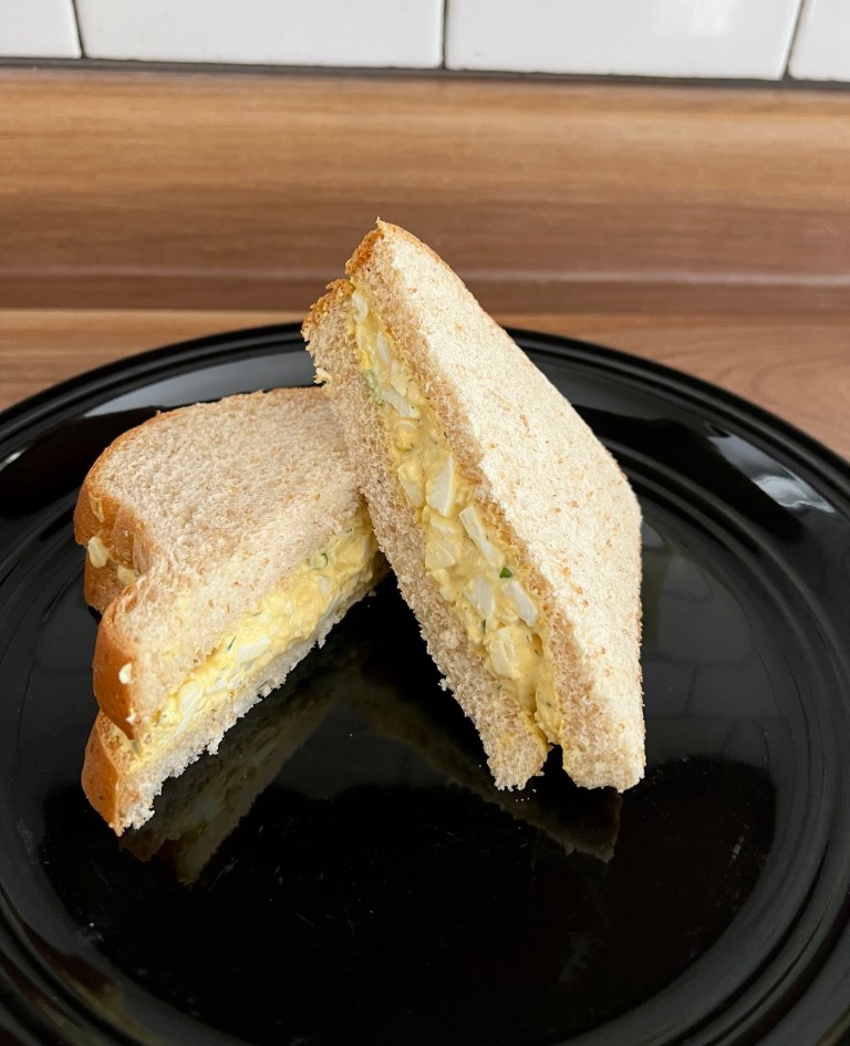 An egg salad sandwich that's been cut in half and sitting on a black plate