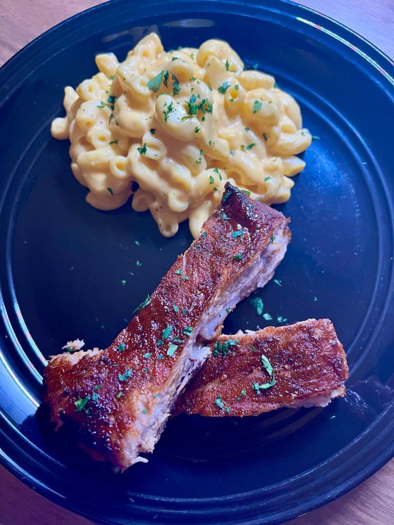 BBQ ribs on a black plate with a side of mac and cheese