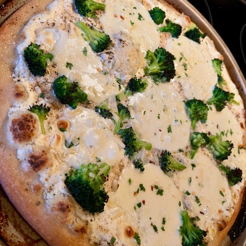 White pizza with broccoli on a round pizza pan