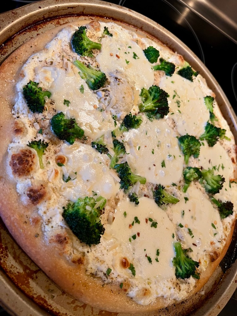 White pizza with broccoli on a round pizza pan