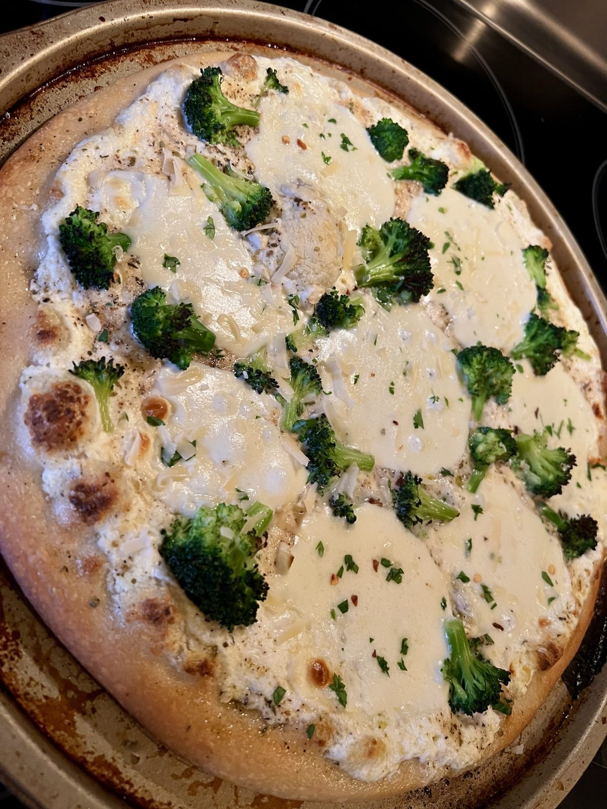 White pizza with broccoli on a round pizza pan