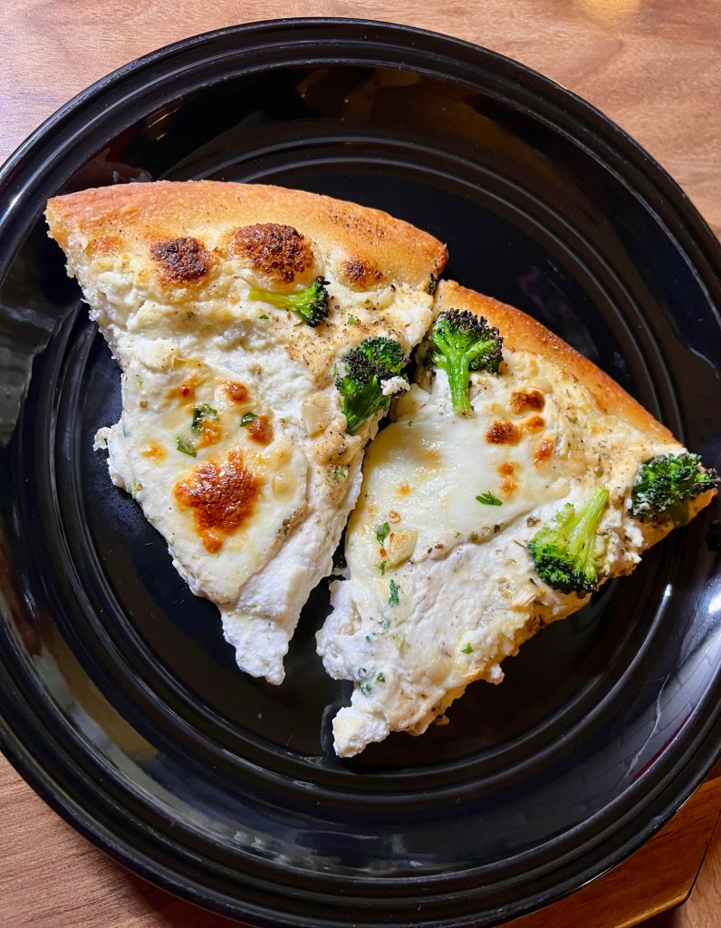 Two slices of white pizza with broccoli on a black plate