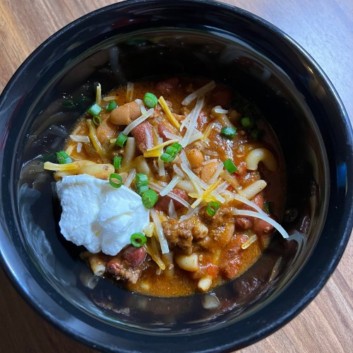 Crockpot chili in a black bowl on a wooden counter