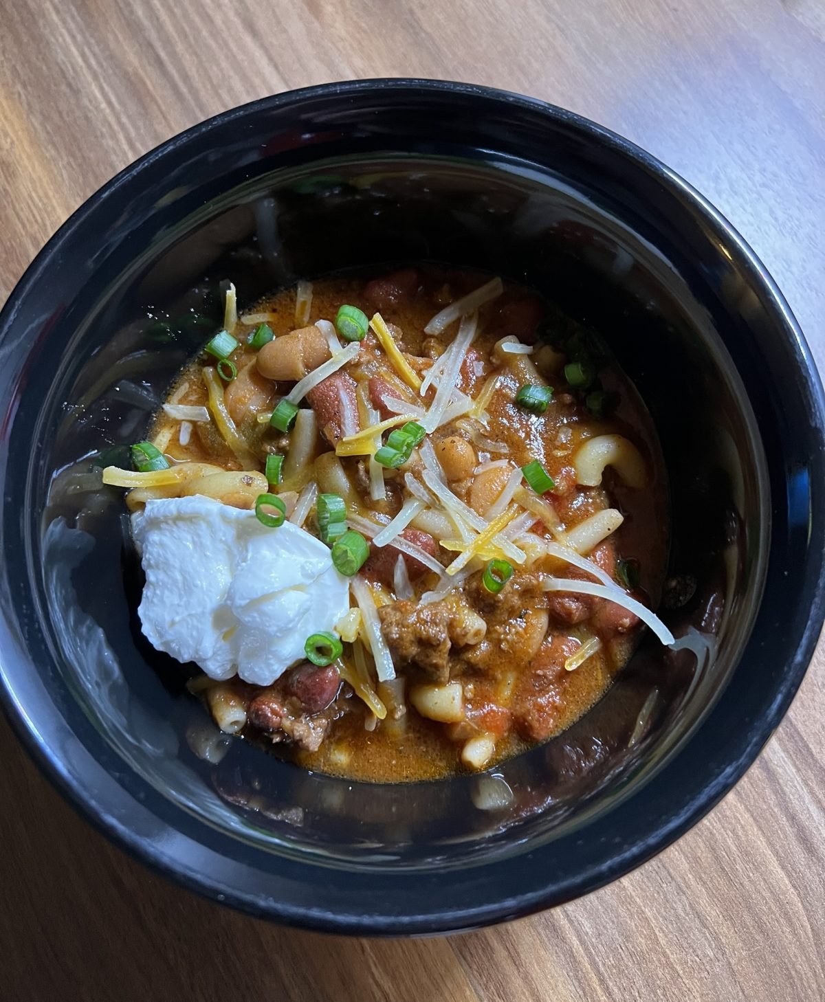 Crockpot chili in a black bowl on a wooden counter