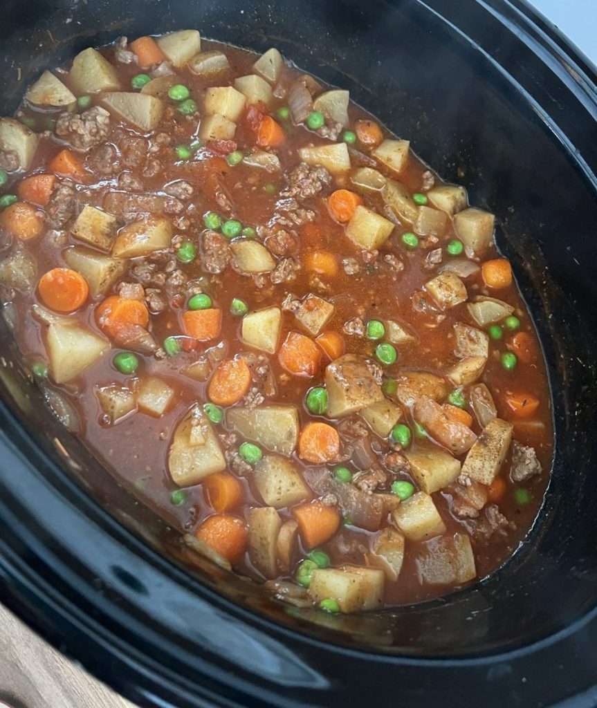 Hamburger stew in a large crockpot on a wooden countertop