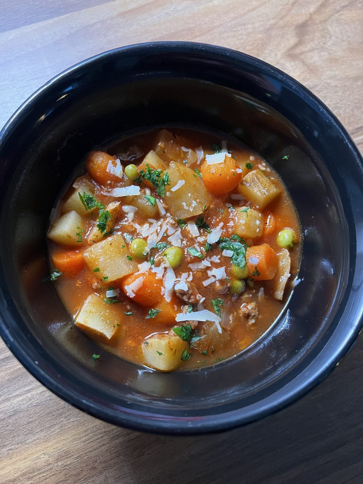 Hamburger Stew in a black bowl on a wooden counter