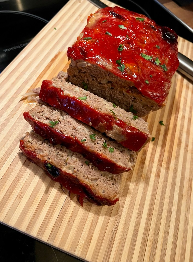 Meatloaf with a ketchup glaze on a wooden cutting board with a knife nearby