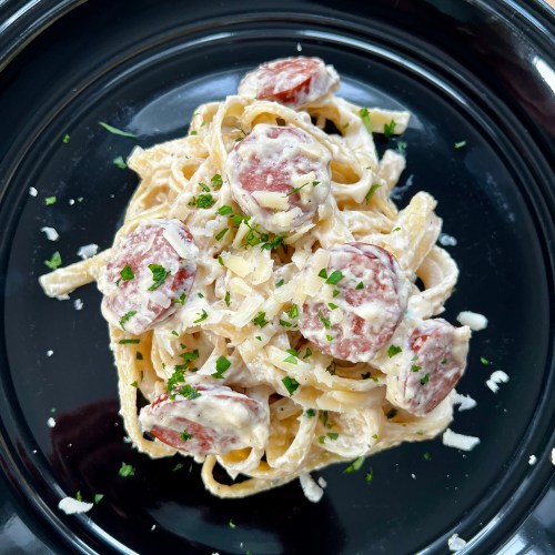Garlic Sausage Alfredo on a black plate on a wooden table