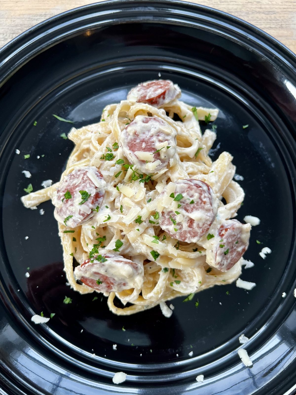 Garlic Sausage Alfredo on a black plate on a wooden table