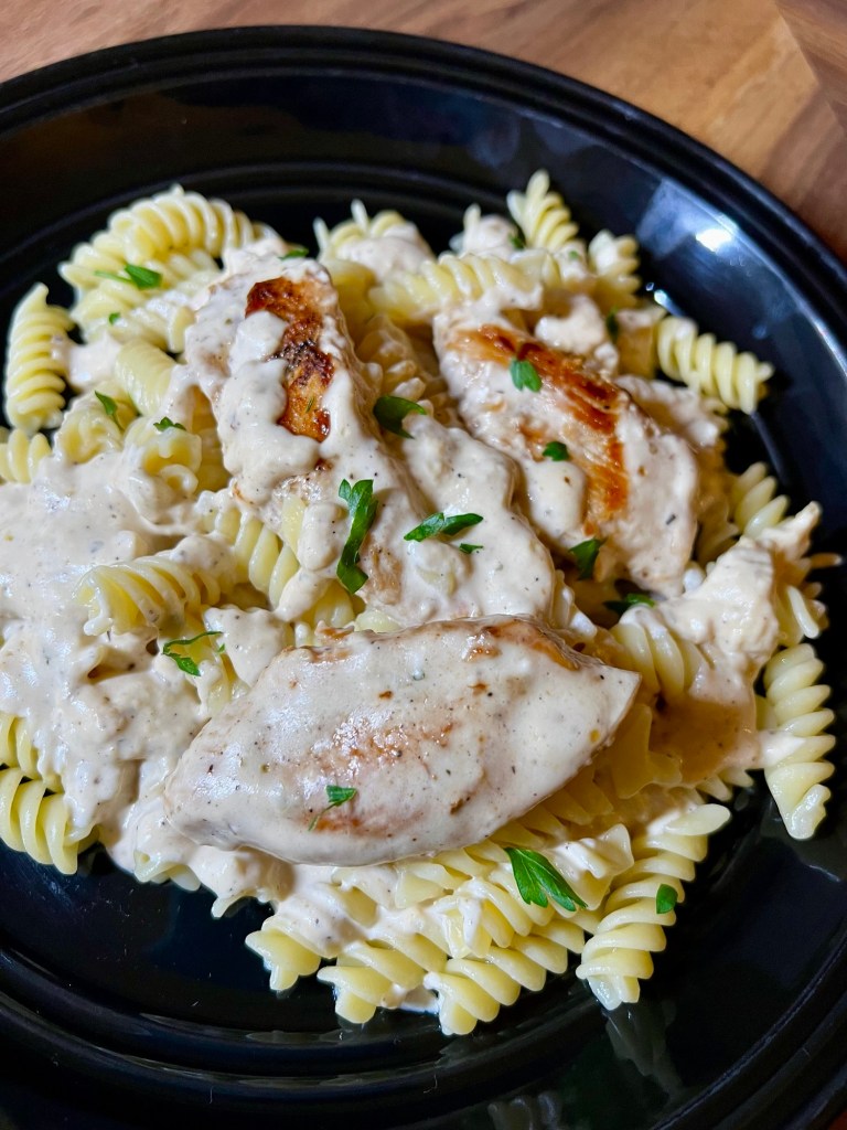 Creamy mustard chicken and pasta on a black plate on a wooden countertop