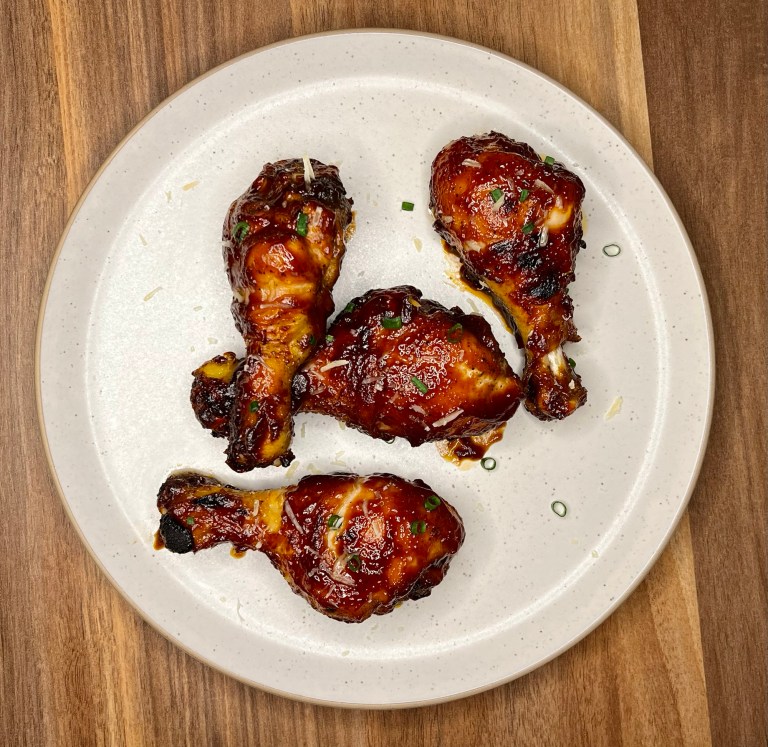BBQ chicken drumsticks on a white plate on a wooden counter