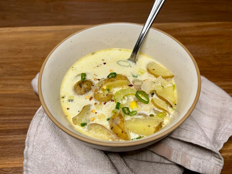Fish chowder in a white bowl with a spoon in it on a wooden counter