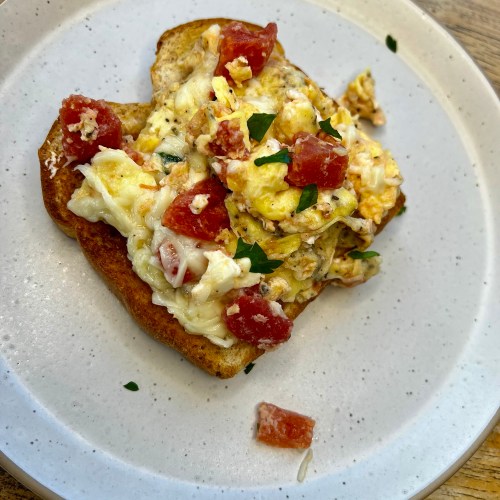 Tomato and feta scrambled eggs on a white plate on a wooden table