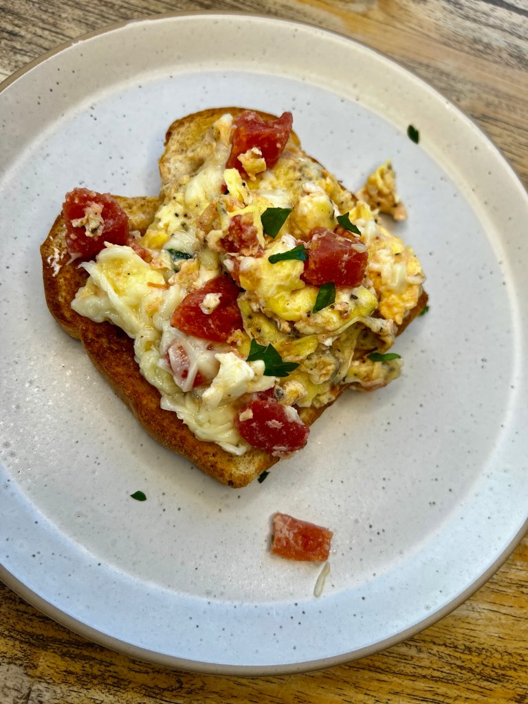 Tomato and feta scrambled eggs on a white plate on a wooden table