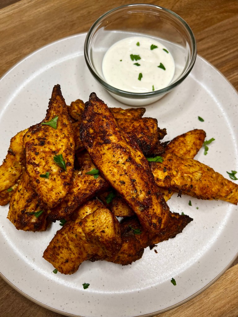Air fryer chicken tenders on a white plate with a small dish of ranch next to it