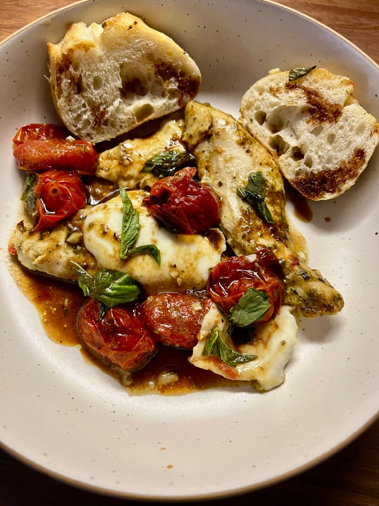 Caprese Chicken in a white bowl with some bread on the side and balsamic drizzle on top