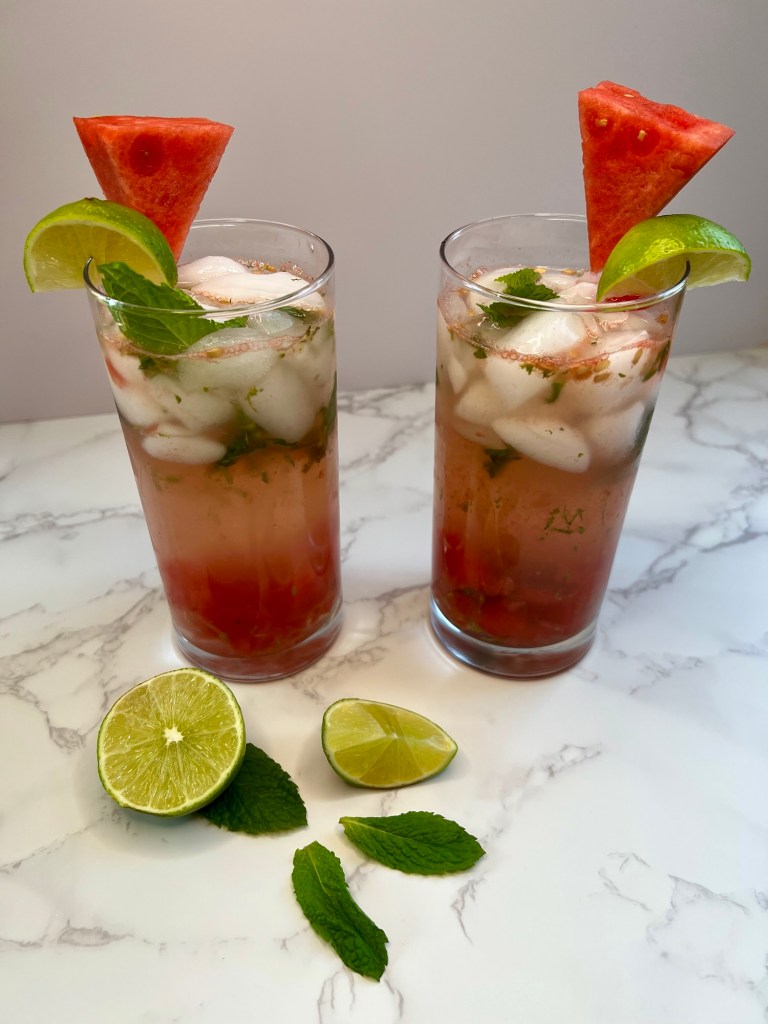 wo Watermelon Mojitos on a marble counter with some lime and mint nearby
