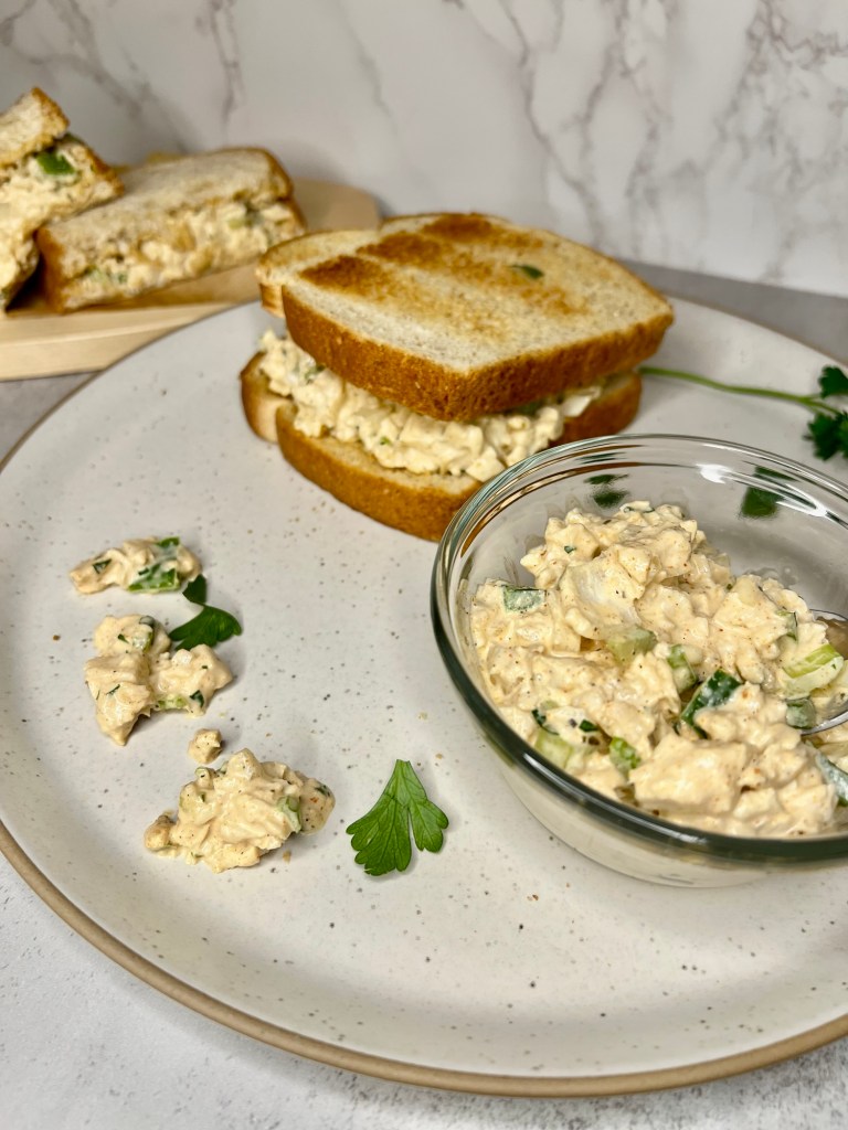 A Cajun Chicken Salad sandwich on a white plate with a dish of the salad next to it