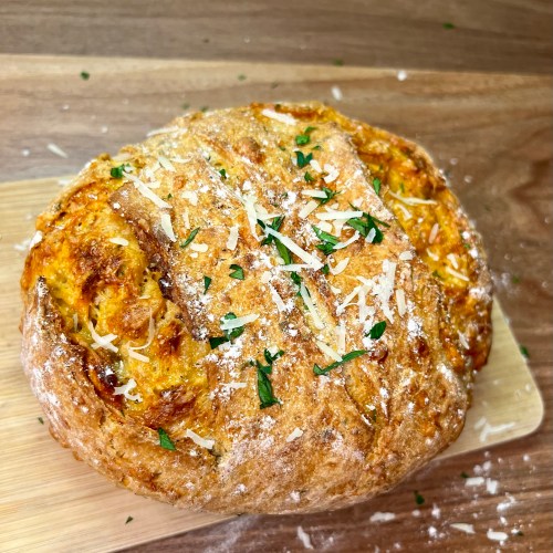 Herb and Cheese bread on a wood cutting board on a wood counter with some flour, parsley, and parmesan on it