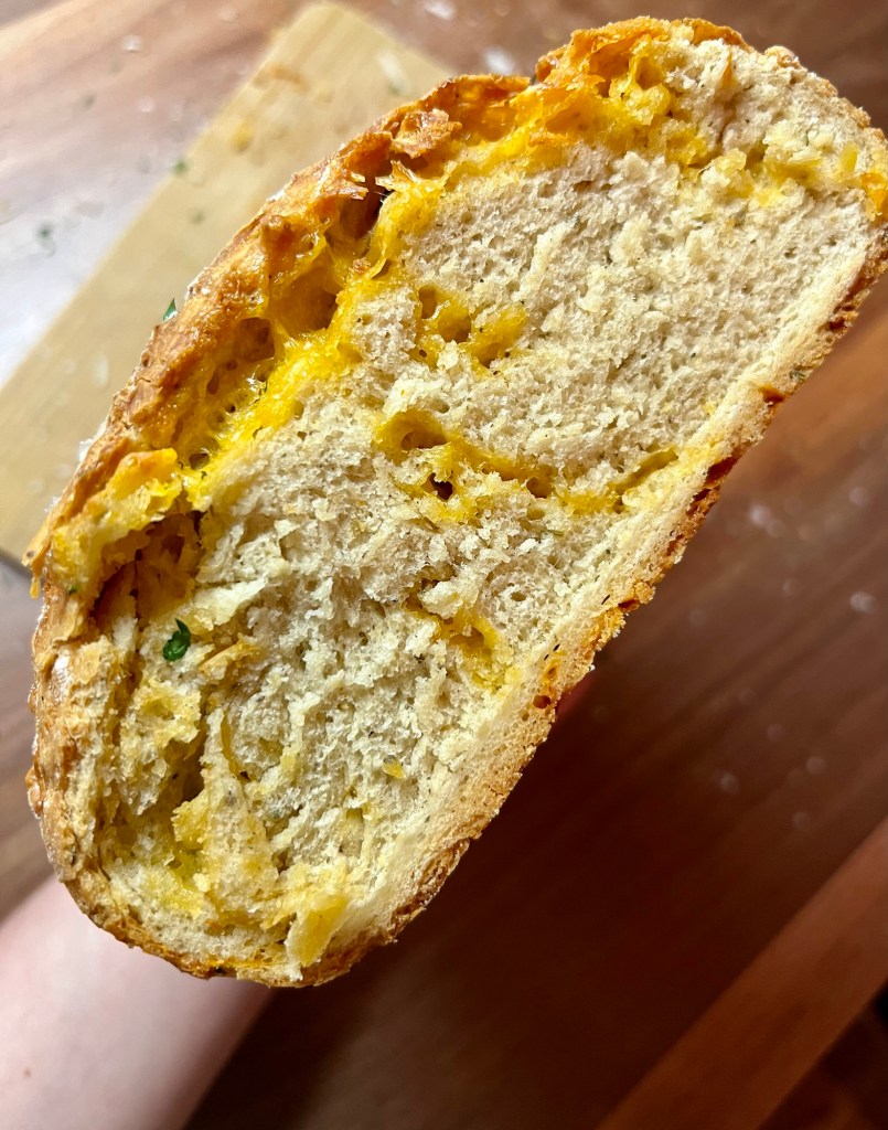 Herb and cheese bread that's been sliced to show the middle and a hand holding it up