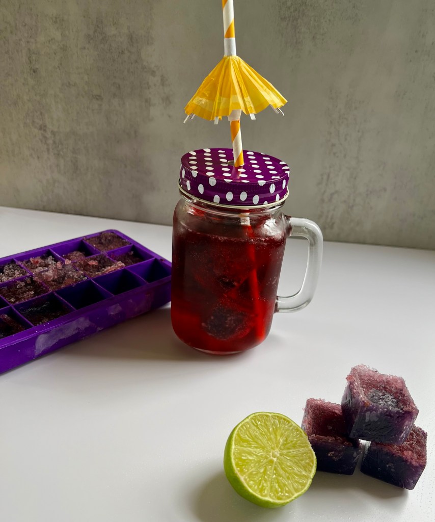 Boozy cubes with some lime next to it and a drink made with them behind it, with an ice cube tray sitting next to it
