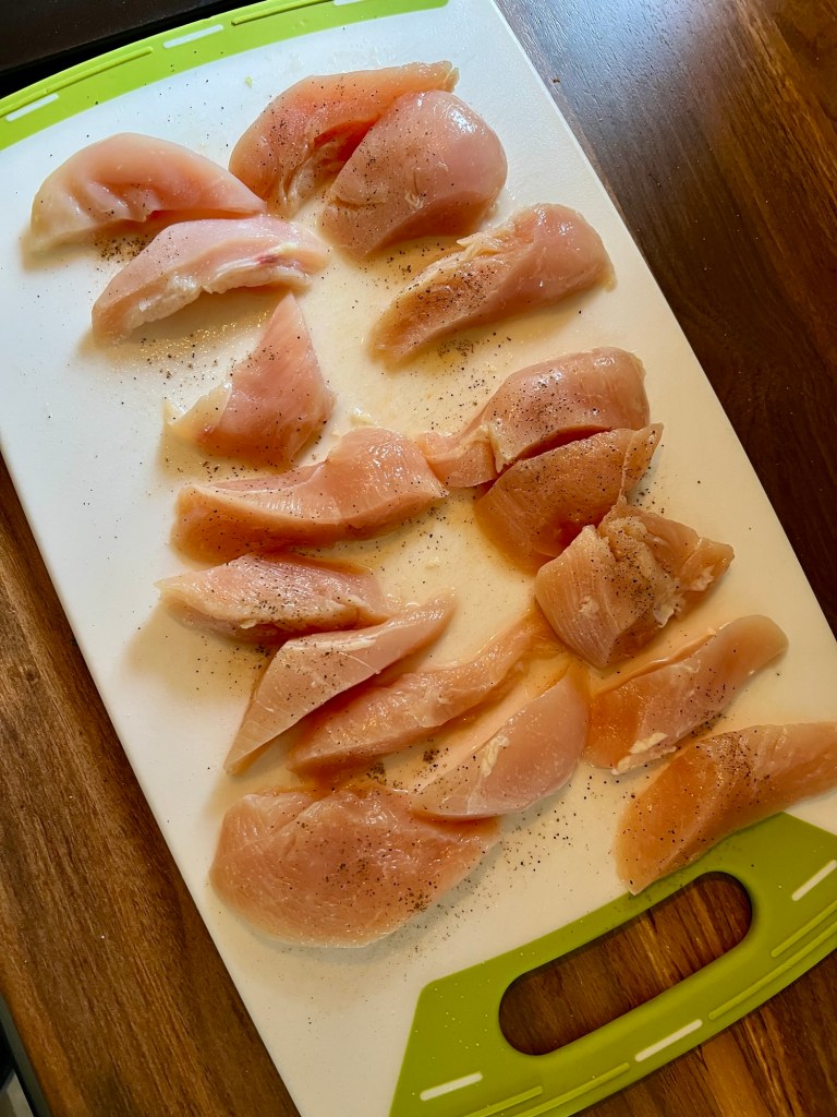 Chicken cut into tenders on a cutting board, with seasonings on top