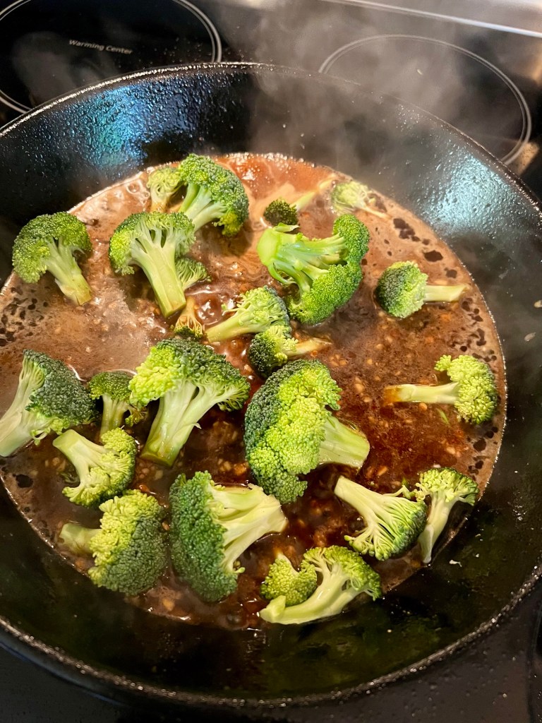 Broccoli and sauce cooking in a skillet on the stove