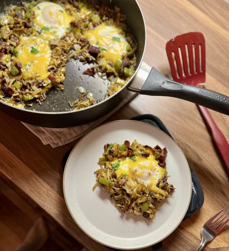 Bacon Breakfast Skillet in a skillet on a wooden counter with a white plate of it nearby and a spatula