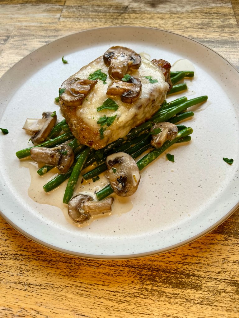 Mushroom Swiss Pork Chops with green beans on a white plate on a wood table