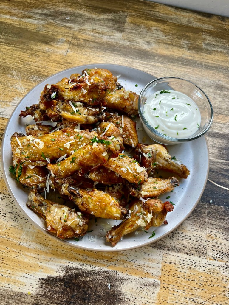 Parmesan Garlic Wings on a white plate with a ramekin of ranch sauce on a wood table