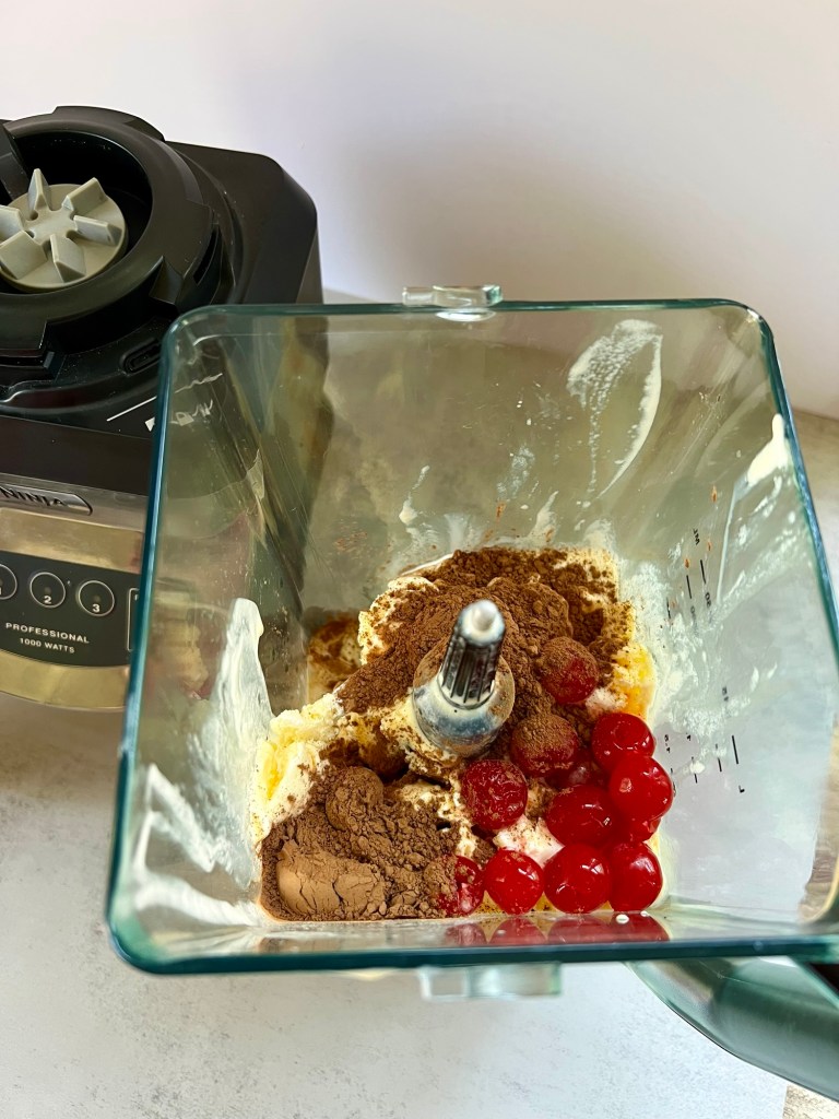 Cherries, cocoa powder, ice cream, coffee, and cream in a blender