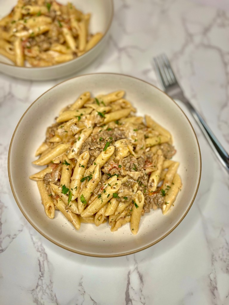 Beefy French Onion Pasta in a white bowl with a fork next to it on a marble counter