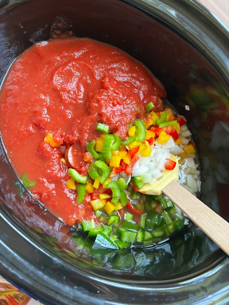 A crockpot filled with fresh veggies, broth, crushed tomatoes, and sausage