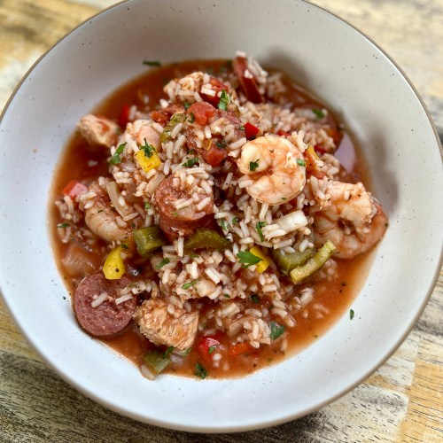 A white bowl filled with Jambalaya on a wooden table