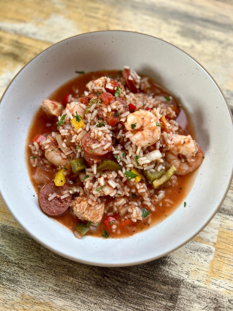 A white bowl filled with Jambalaya on a wooden table