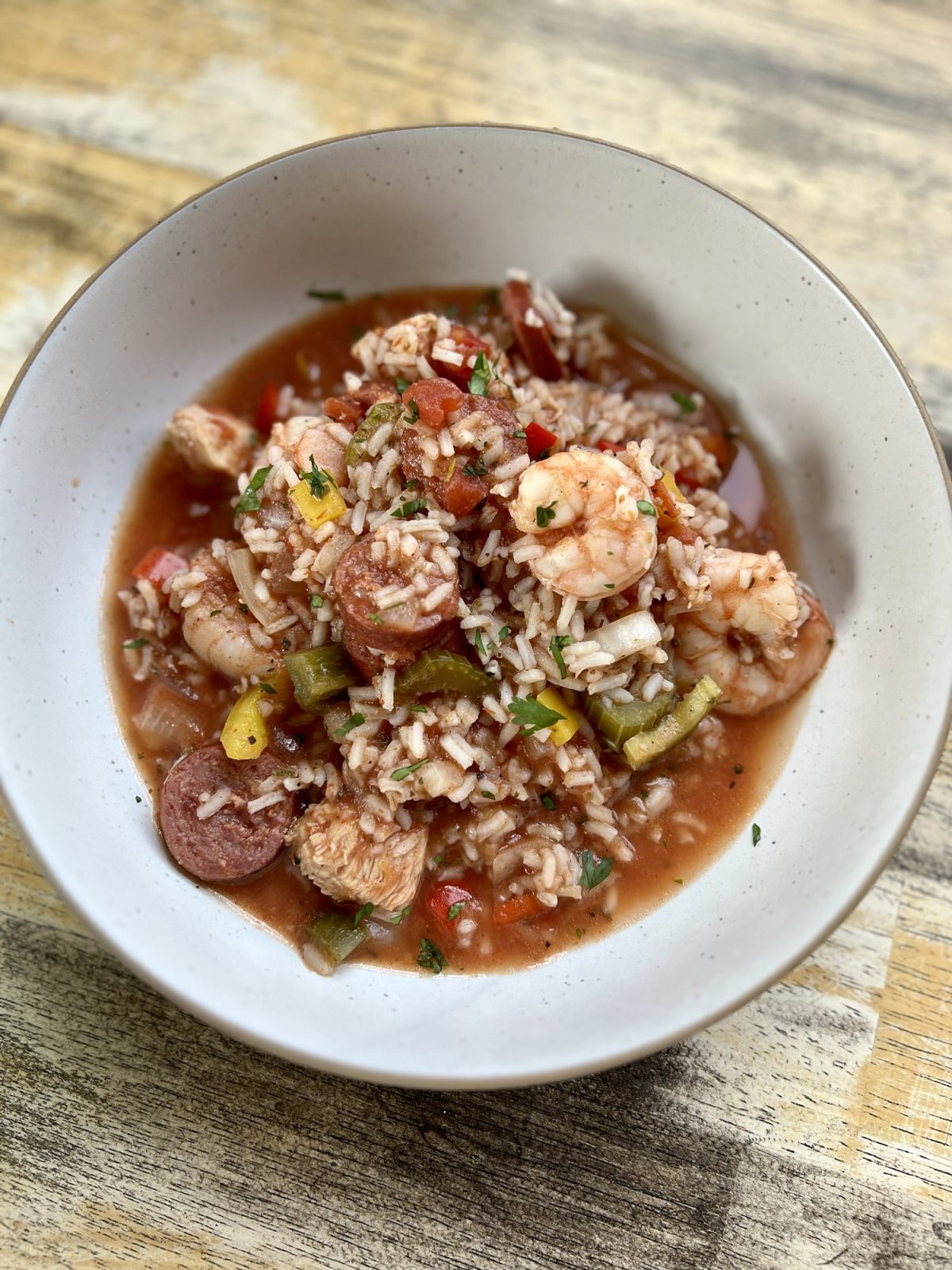 A white bowl filled with Jambalaya on a wooden table