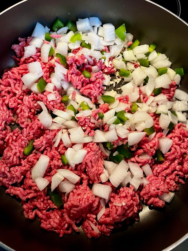 Ground beef and veggies cooking in a large skillet on the stove