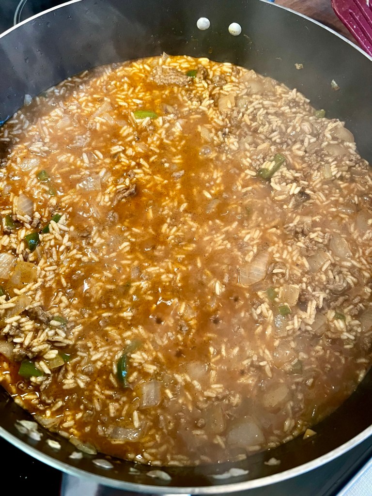 A large skillet filled with veggies, beef, broth, and rice cooking on the stove