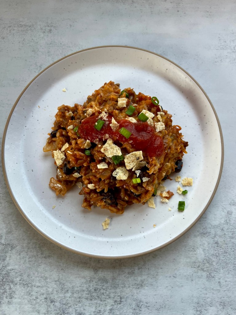 Burrito bake on a white plate with some green onion, tortilla chips, and salsa on top