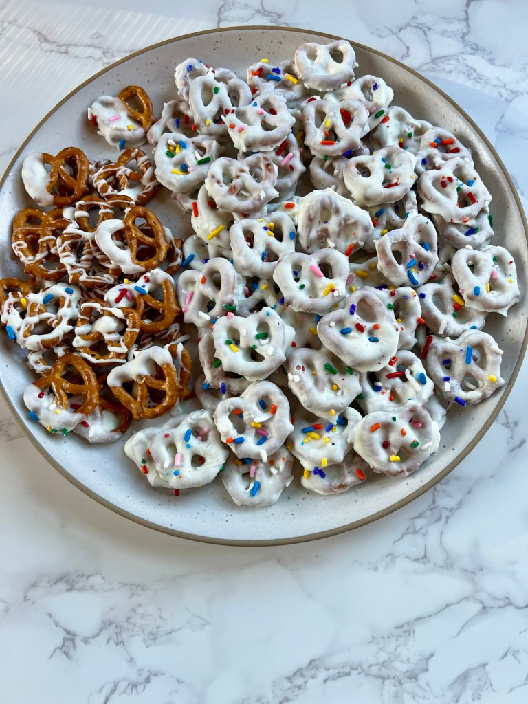 White chocolate covered pretzels on a white plate on a marble counter