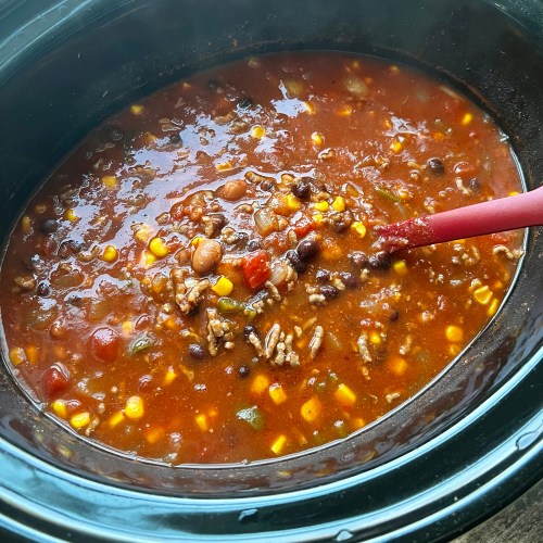 Crockpot taco soup in a large crockpot on a wooden table, with a red spoon scooping some